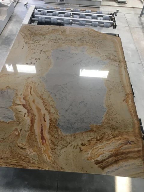 A Mojave Mural sandstone slab on a processing line, with a gray center and sweeping cream, gold and brown bands.